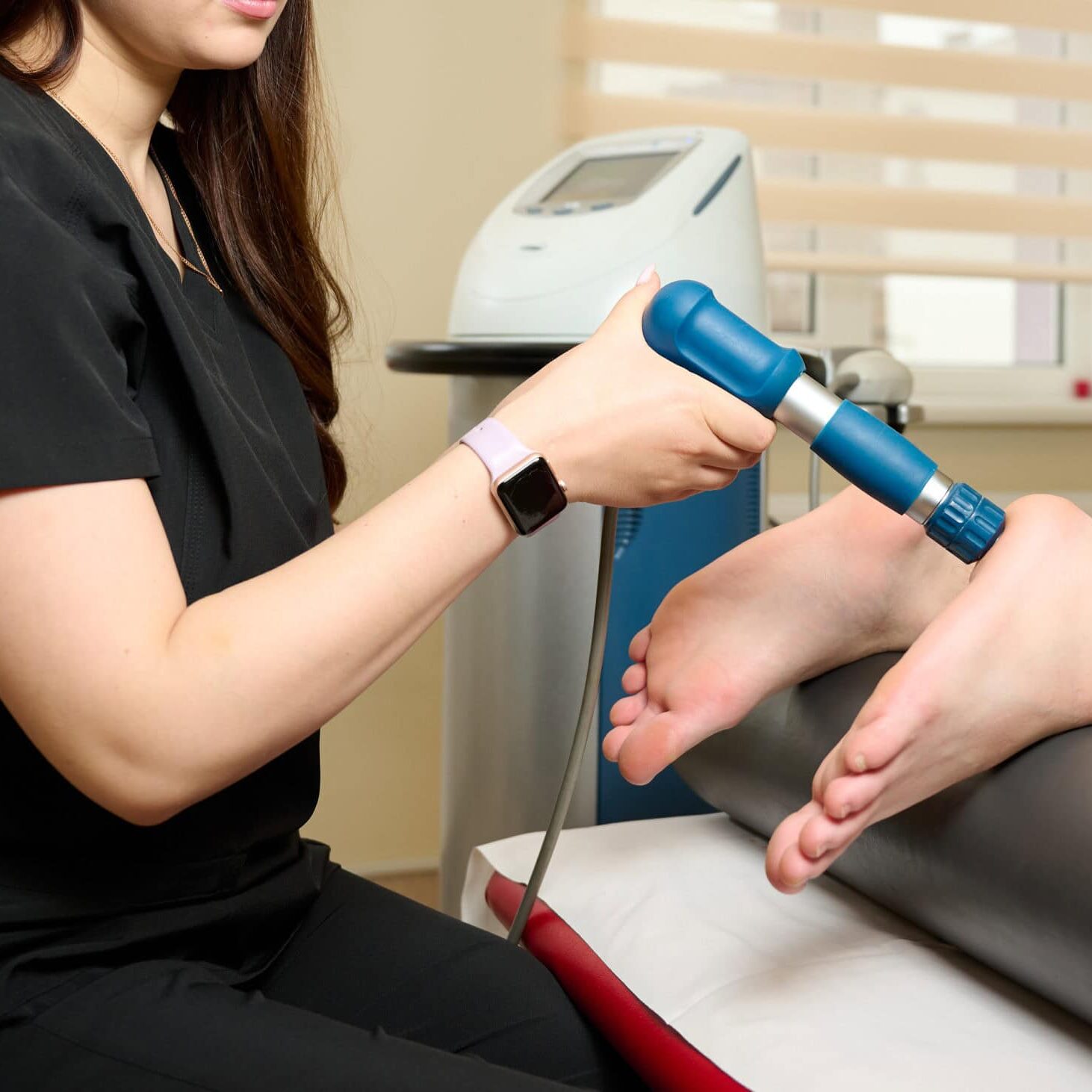 Physical therapy of foot with acoustic shock waves. Close up view of doctor performing shock wave therapy procedure on leg. Female doctor holding pneumatic shock wave therapy machine for pain relief.