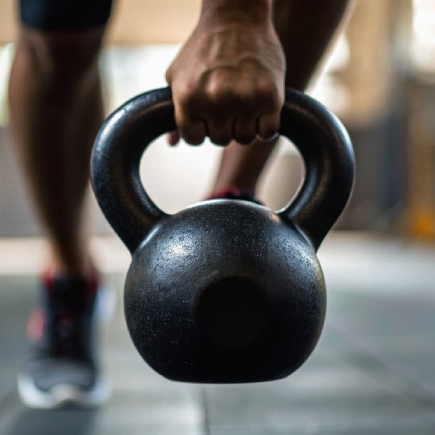 A person lifting a kettlebell in a gym, showcasing strength and fitness in a dynamic workout setting.